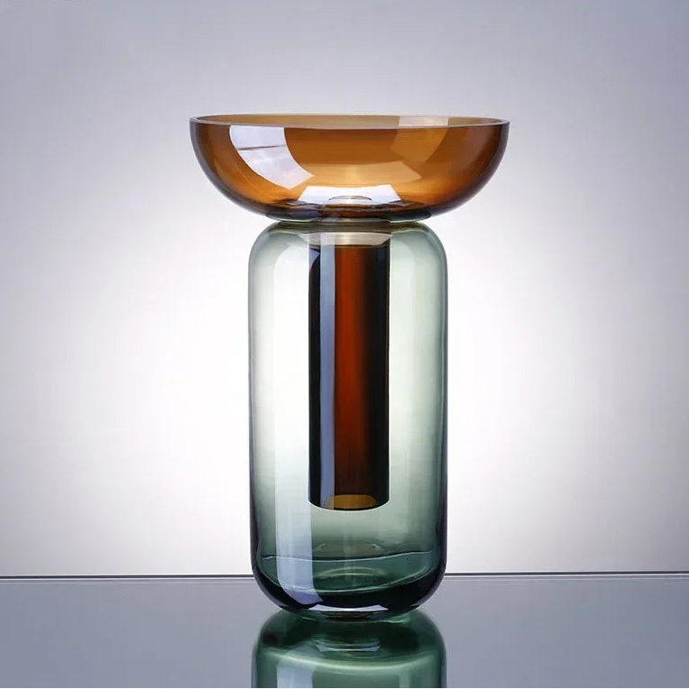 Glass vase with gradient color from amber to green on a reflective surface.